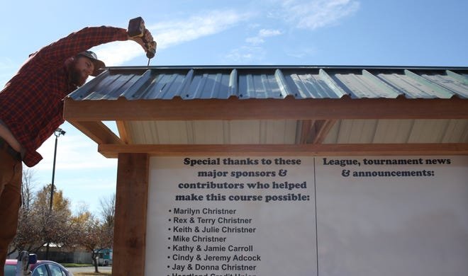 Handyman Andrew Nelson installs a roof over the Keith Christner Family disc golf course sign near the entrance of Rice Park that shows the layout of the new 18-hold disc golf course. The course, intended for beginning players and families was installed over the last two months through the efforts of the Christner family.